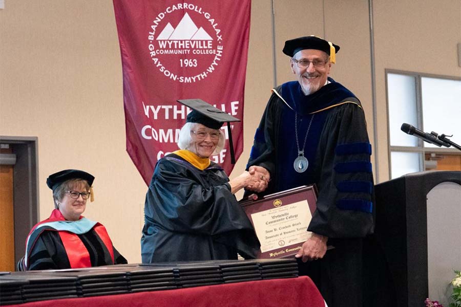 A woman in a graduate's cap and gown is being handed a degree by Wytheville Community College's president. 