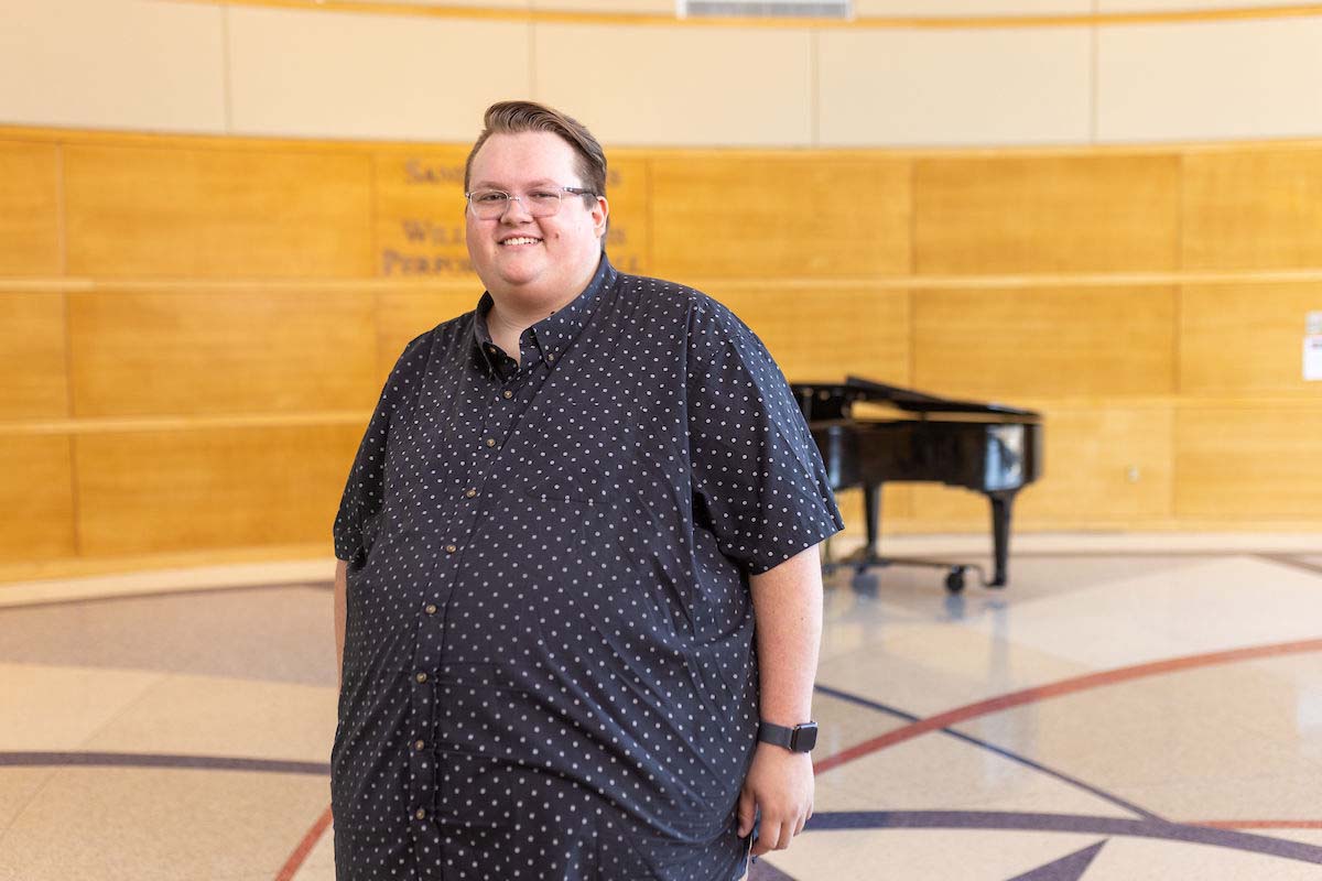 A graduate student in music stands before a grand piano in the lobby of the Covington Center