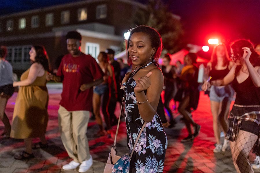 A group of students dance under colorful campus lights