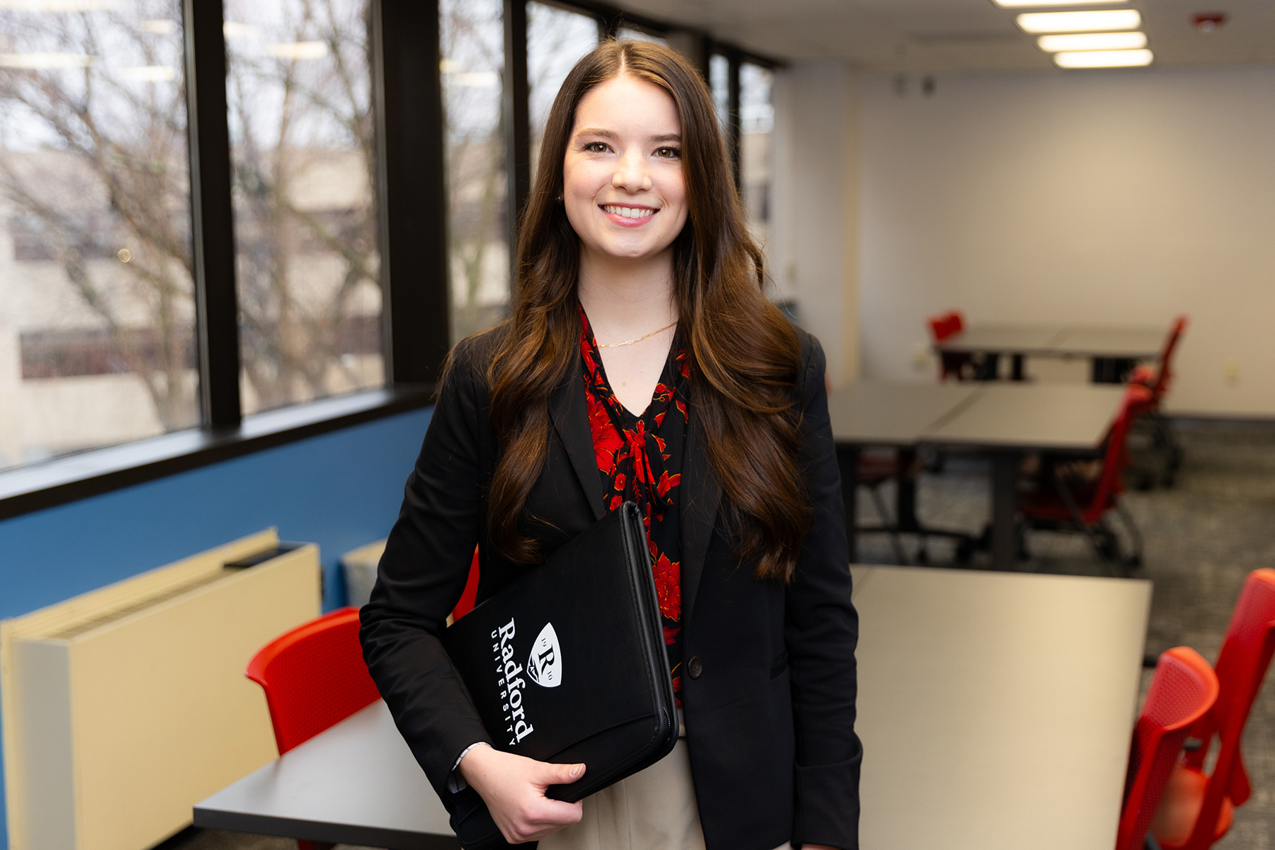 student carrying a Radford folder smiling in a classroom