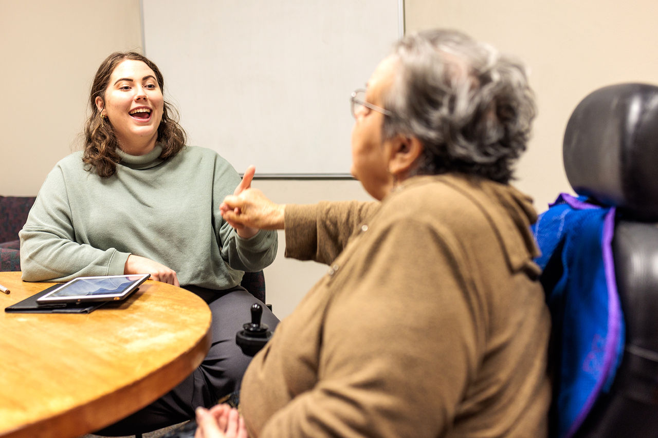 student with patient in wheelchair at a table smiling at each other