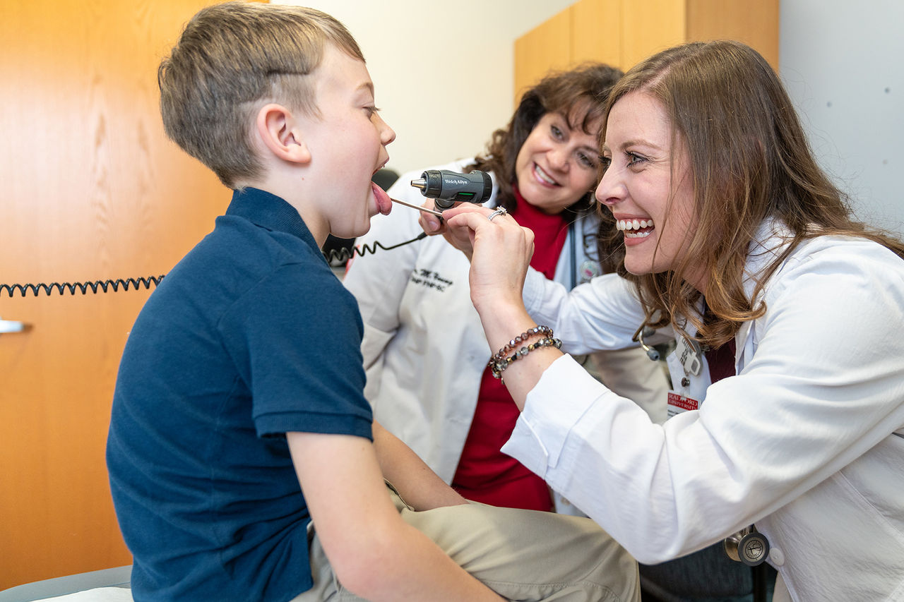 child on a patient table with his mouth open while nurse looks into his mouth