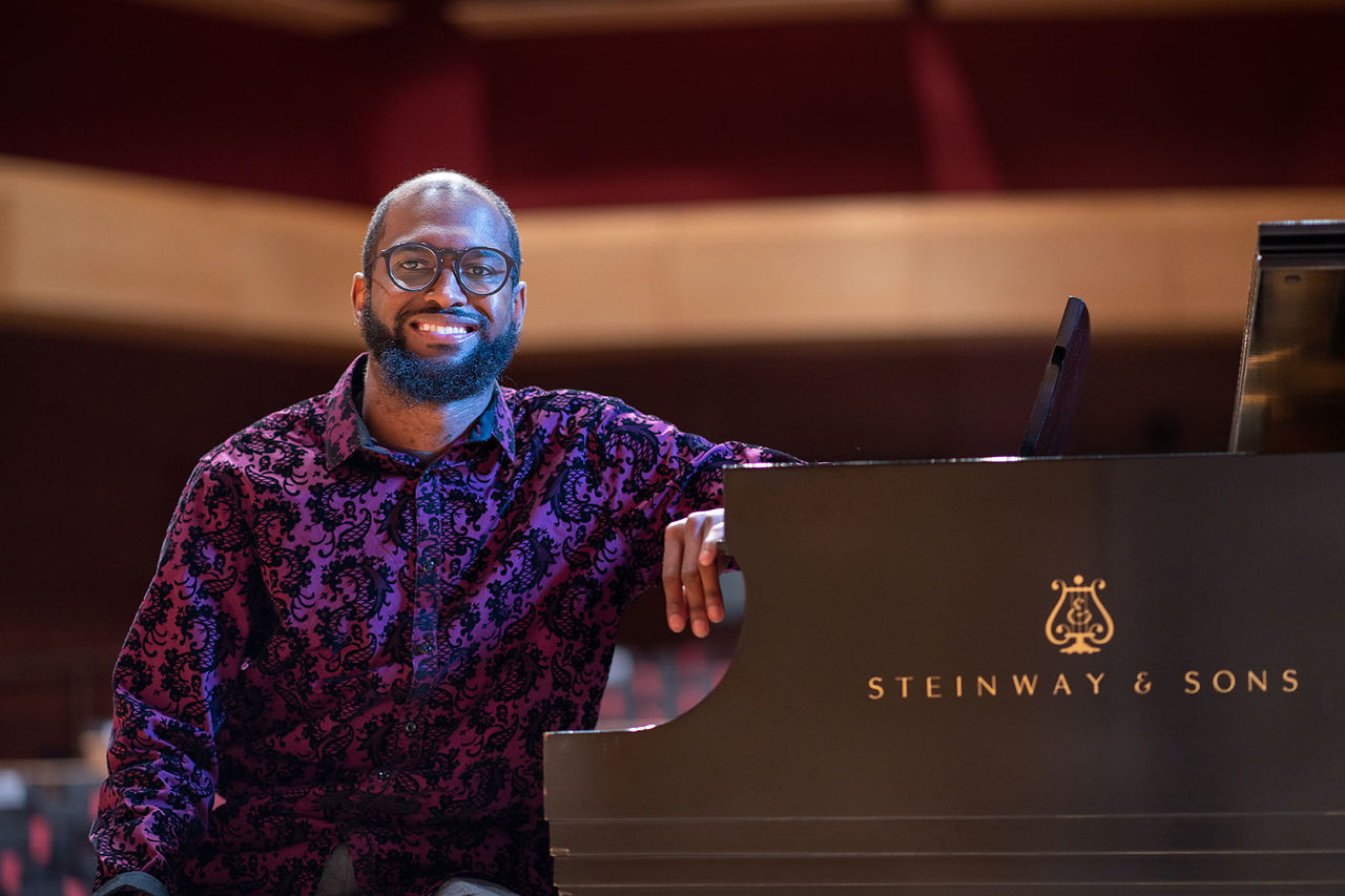 student smiling sitting on a bench of a steinway and sons piano 